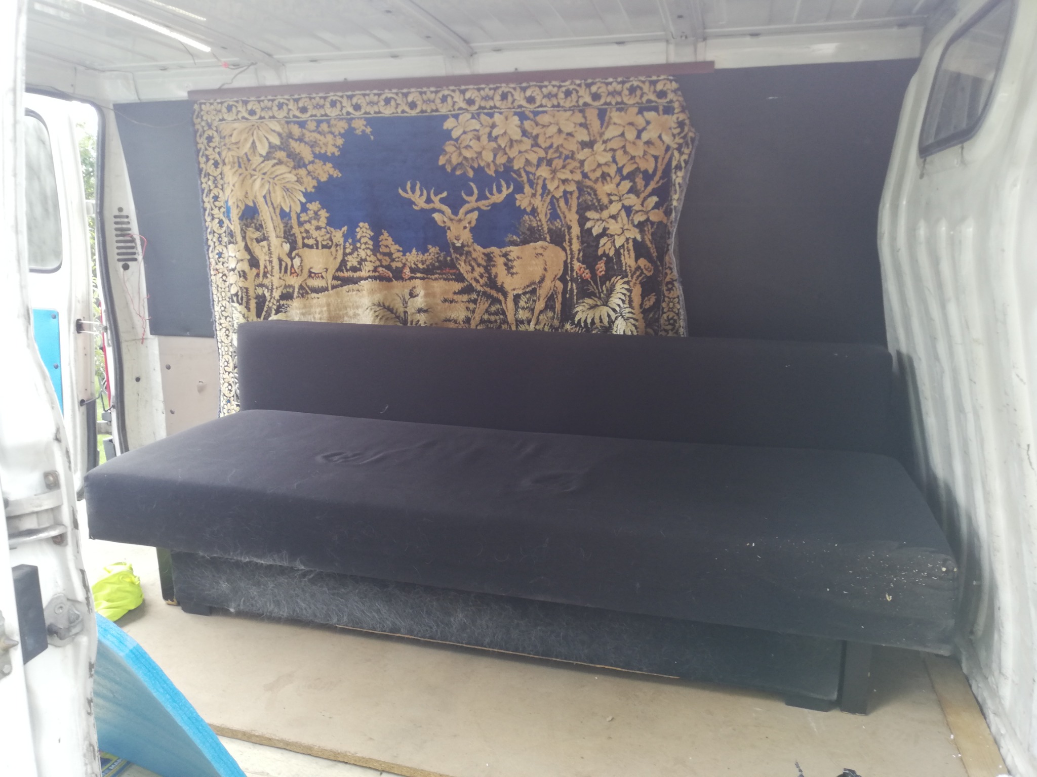 Wnętrze busa w Białych Błotach z załadowaną czarną sofą i dekoracyjnym gobelinem z motywem jelenia na ścianie, przygotowane do transportu.