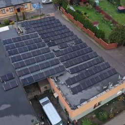 EliteEnergy - Widok z góry na dach budynku z zainstalowanymi panelami fotowoltaicznymi; widoczny zaparkowany bus serwisowy i pracownicy.