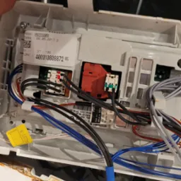 Wnętrze panelu sterowania pralki z widocznymi przewodami, złączami i etykietą z numerem modelu 859333349050 oraz datą produkcji 29.05.2017. Widoczne ślady korozji na obudowie.