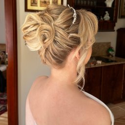 Glow District Dominika Rzymyszkiewicz - Elegancka fryzura ślubna z upięciem i ozdobną spinką, widok z tyłu na tle wnętrza z drewnianymi meblami.