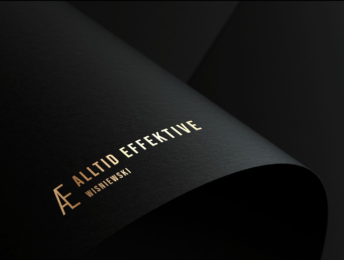 Czarny, teksturowany papier zwinięty w łuk, z wytłoczonym złotym logo 'Æ ALLTID EFFEKTIVE WISNIEWSKI'.
