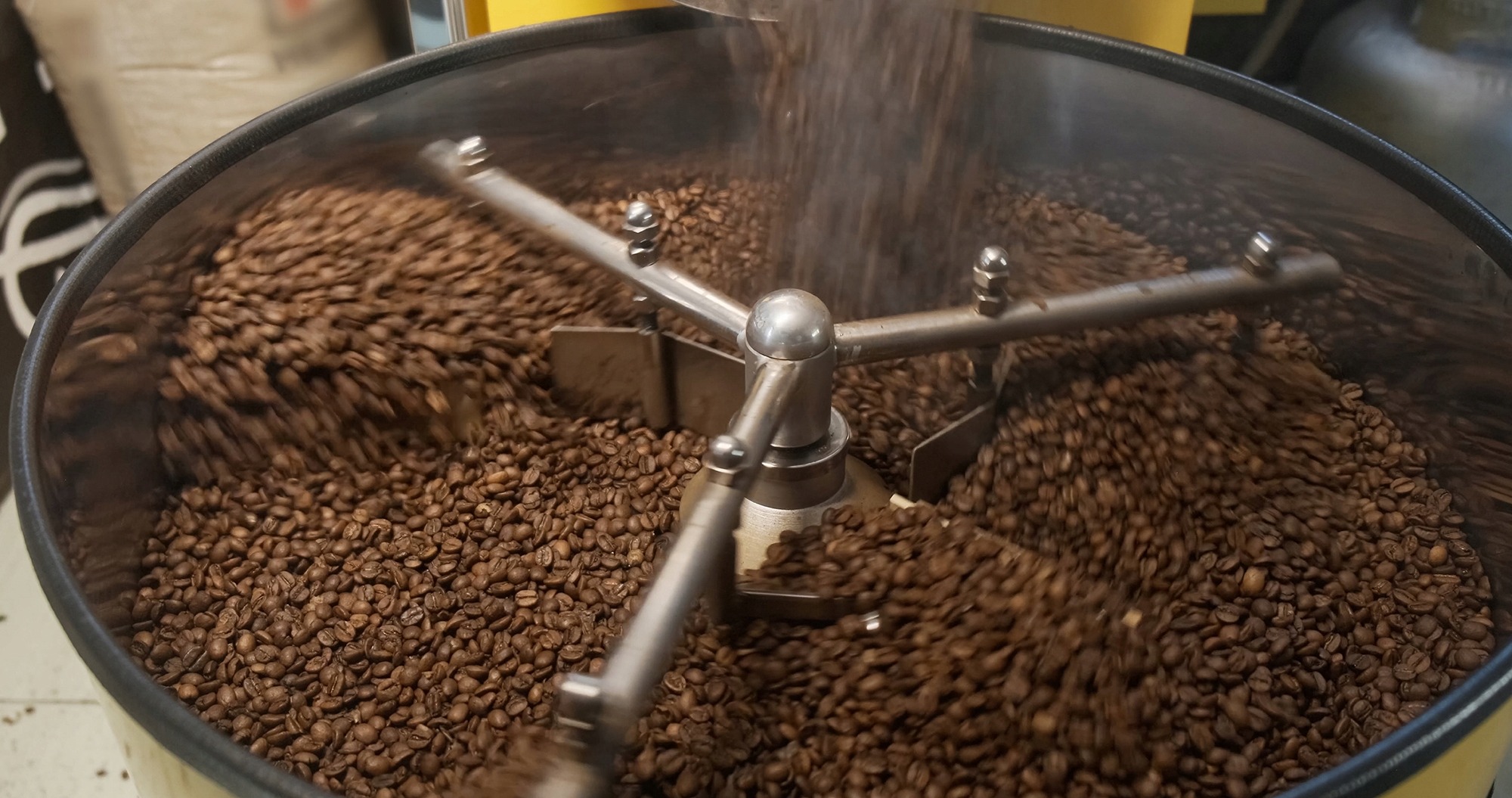 Proces prażenia ziaren kawy w metalowym bębnie z mieszadłem, ukazujący ruch i aromat świeżo palonej kawy. Dynamiczne ujęcie z bliska.