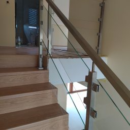 Volodymyr Mikhalets Amix balustrady nierdzewne - Szczegółowe ujęcie schodów z drewnianymi stopniami i balustradą szklaną mocowaną do słupków ze stali nierdzewnej; widoczne niedokończone prace wykończeniowe w tle.