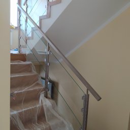 Volodymyr Mikhalets Amix balustrady nierdzewne - Szklana balustrada ze stalowymi słupkami i poręczą na drewnianych schodach, zabezpieczonych folią ochronną podczas montażu.
