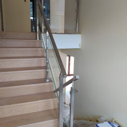 Volodymyr Mikhalets Amix balustrady nierdzewne - Szczegółowe ujęcie drewnianych schodów z nowoczesną balustradą ze szkła i stali nierdzewnej, widoczne ślady prac wykończeniowych.