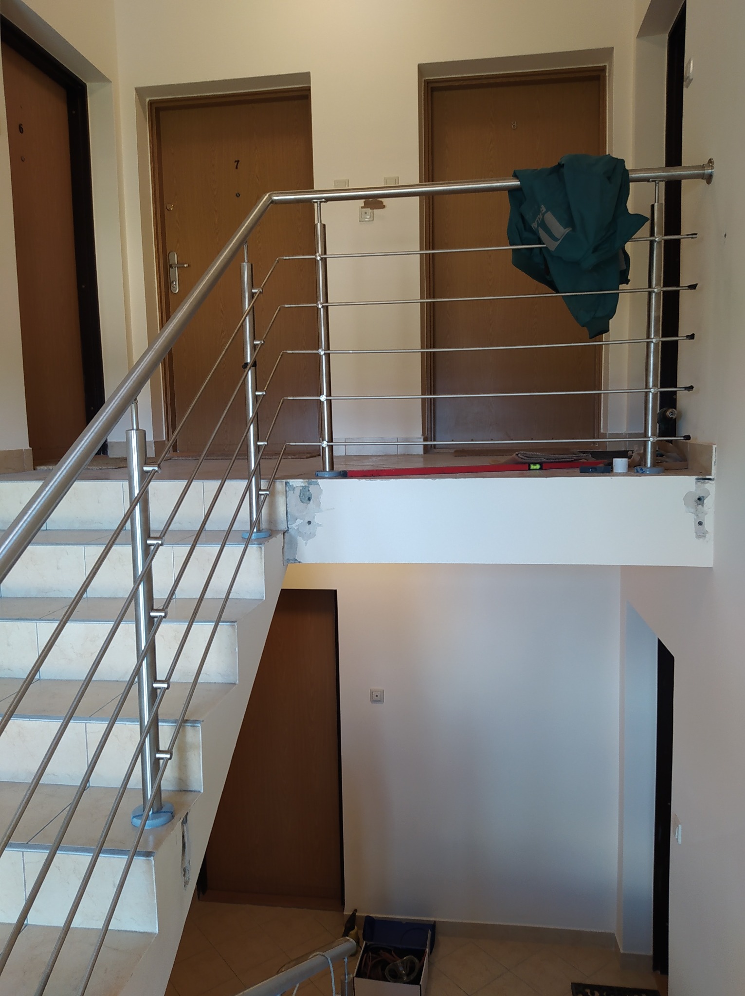 Montaż stalowej balustrady wewnątrz budynku w Krakowie, widoczne schody, narzędzia i ubranie robocze pozostawione na górnej części balustrady.