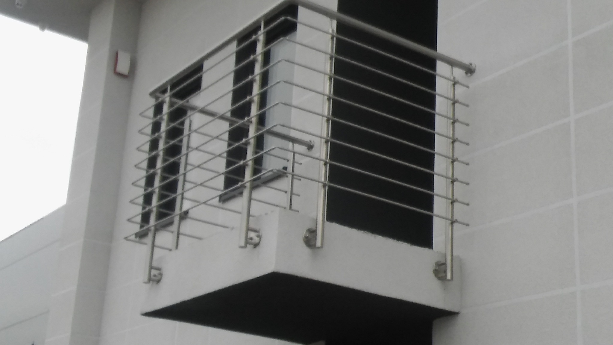 Balkon z nowoczesną, minimalistyczną balustradą ze stali nierdzewnej, mocowaną do ściany z jasnych płytek.