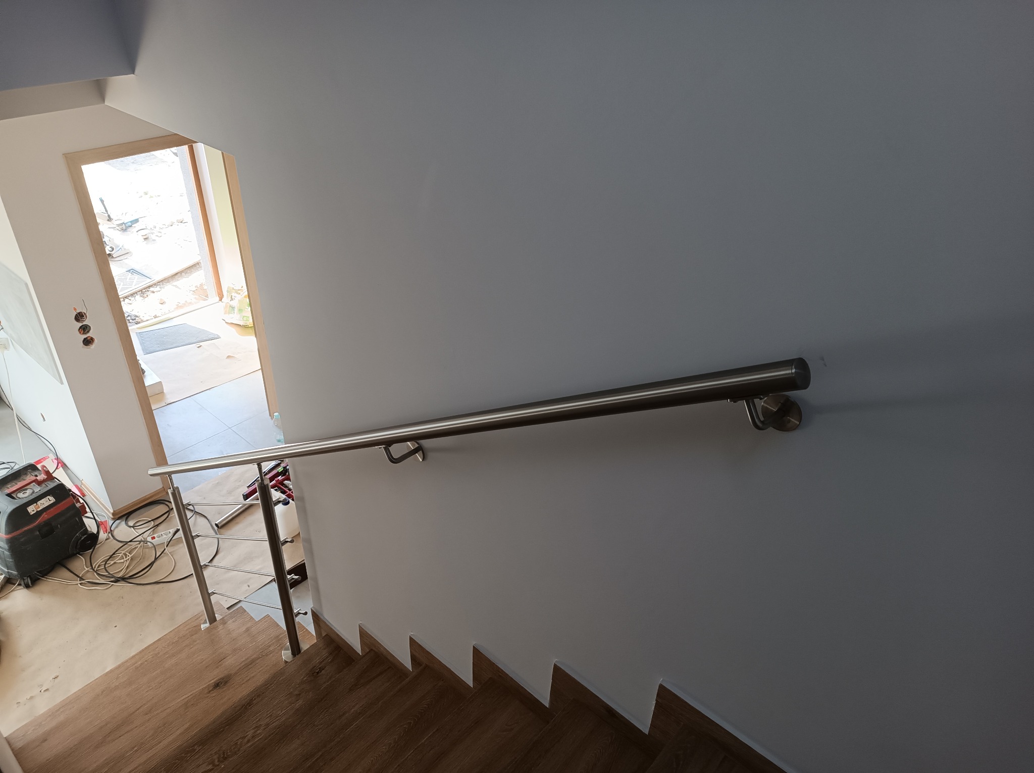 Montaż poręczy ze stali nierdzewnej na schodach z drewnianymi stopniami, widoczny odkurzacz przemysłowy i narzędzia w tle.