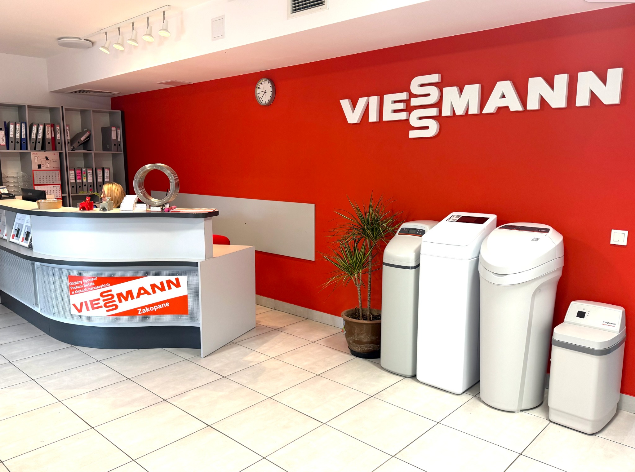 Wnętrze biura z recepcją i ekspozycją urządzeń grzewczych marki Viessmann na tle czerwonej ściany z logo firmy.