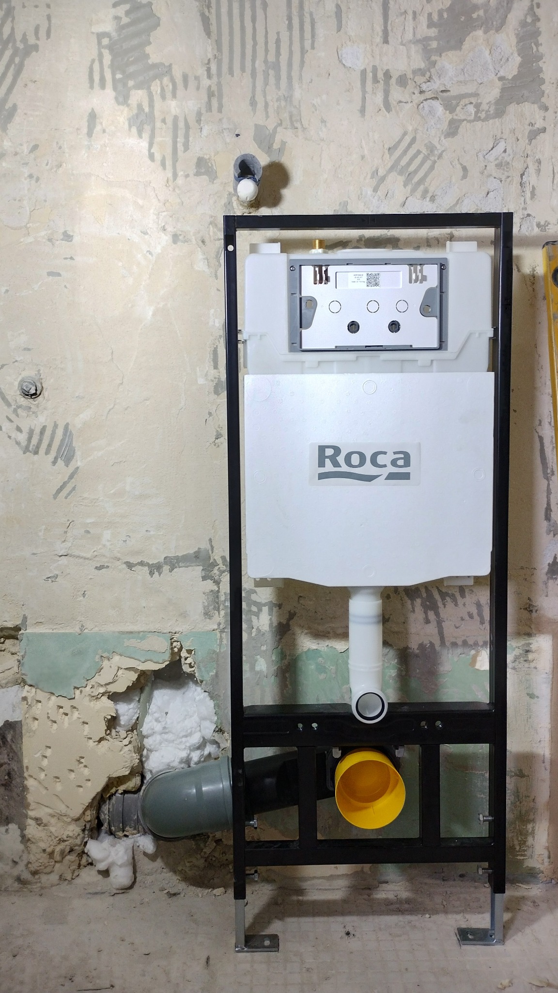 Stelaż podtynkowy WC marki Roca zamontowany na ścianie w trakcie remontu łazienki, widoczne rury kanalizacyjne i fragment ściany z resztkami starej farby.