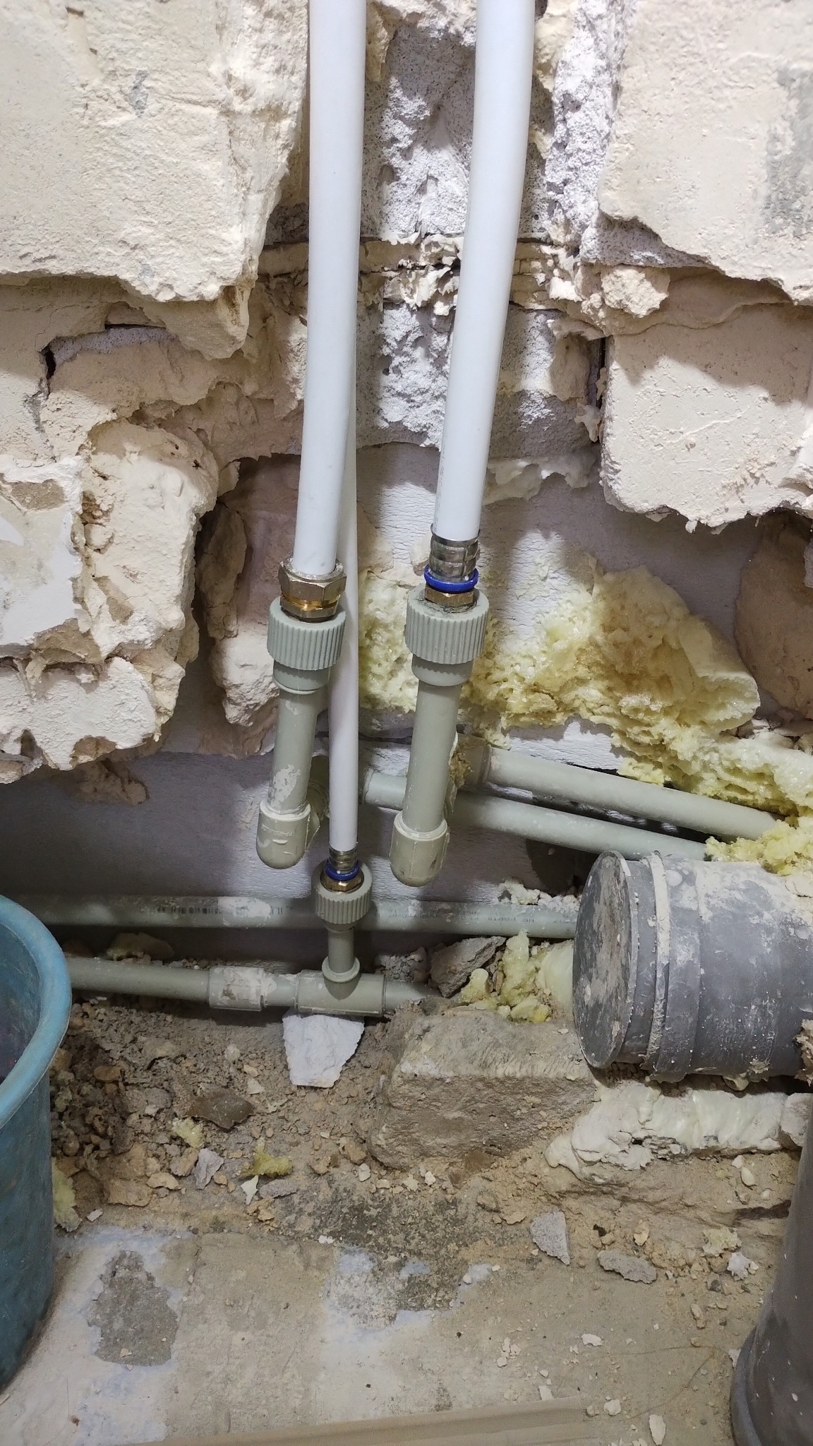 Odsłonięte rury instalacji wodnej w trakcie prac remontowych, widoczne fragmenty ściany z ubytkami i pianką montażową.