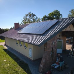 D&S Damian Ślęzak - Montaż paneli na dachu domu jednorodzinnego z ceglaną elewacją; widoczny instalator przy pracy, drabina oparta o ścianę budynku, skrzynka narzędziowa na ziemi.