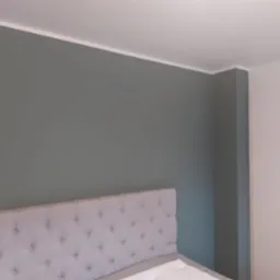 Pomieszczenie po odświeżeniu: ściana w odcieniach szarości, widoczna wezgłowie łóżka z pikowaniem i biała szafa w tle.