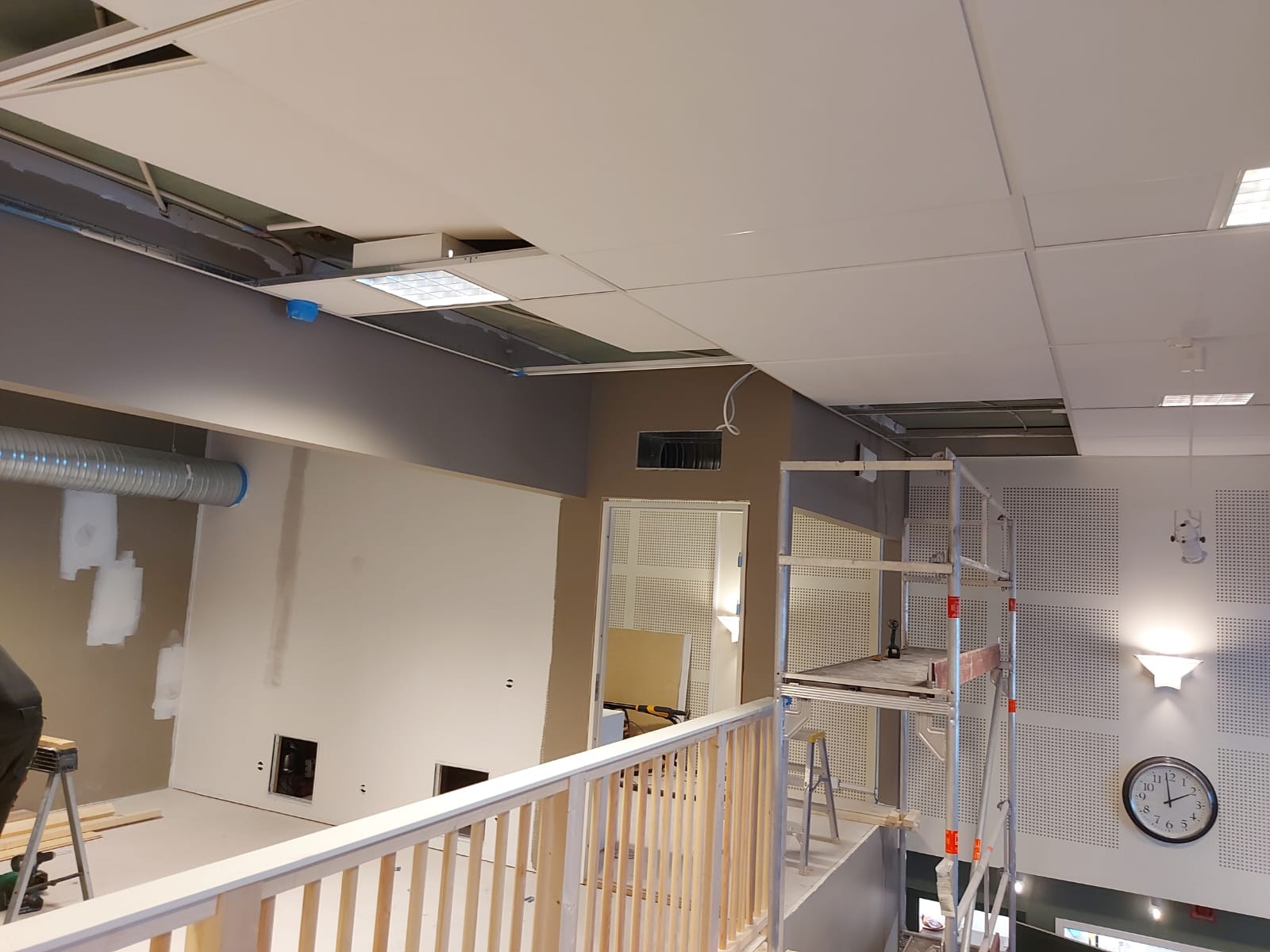 Wnętrze biura w trakcie prac wykończeniowych: szpachlowane ściany, częściowo zamontowany sufit podwieszany, widoczne rusztowanie i instalacje wentylacyjne.