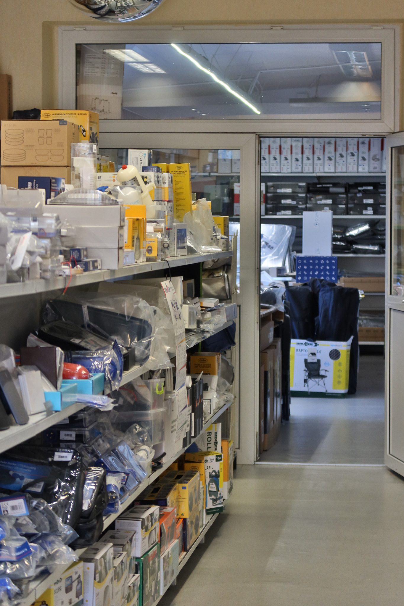 Półki w sklepie z akcesoriami samochodowymi i turystycznymi, widok z perspektywy alejki, różnorodne opakowania produktów, w tle widoczne dalsze regały.