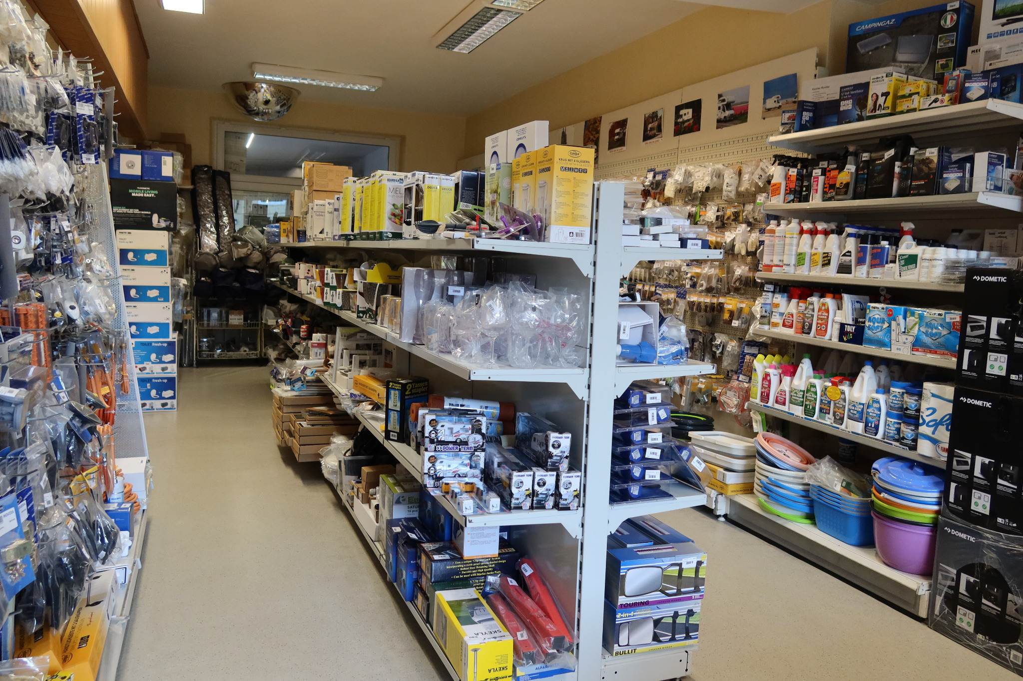 Wnętrze sklepu z akcesoriami motoryzacyjnymi i kempingowymi, regały wypełnione produktami różnych marek, widoczne opakowania akcesoriów do toalet turystycznych, lusterka samochodowe, chemia...