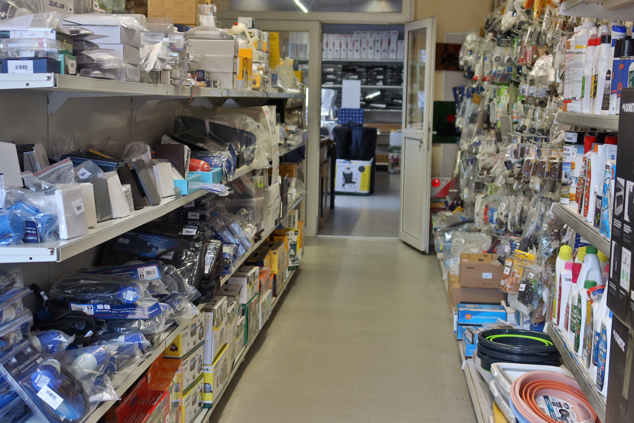 Wnętrze sklepu z akcesoriami motoryzacyjnymi, półki pełne produktów w opakowaniach, widok w głąb sklepu przez otwarte drzwi.