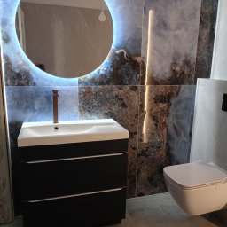 Sap-Tom Instalacje Elektryczne, Wykończenia - Nowoczesna łazienka: czarna szafka z umywalką, okrągłe lustro z podświetleniem LED na tle marmurowych płytek. Minimalistyczna toaleta podwieszana.