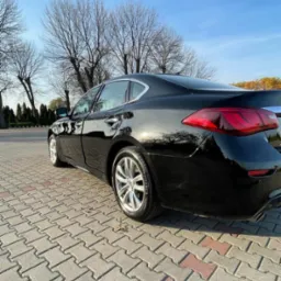 Błyszczący, czarny samochód sedan po detailingu, widoczny z tyłu, zaparkowany na kostce brukowej w słoneczny dzień.