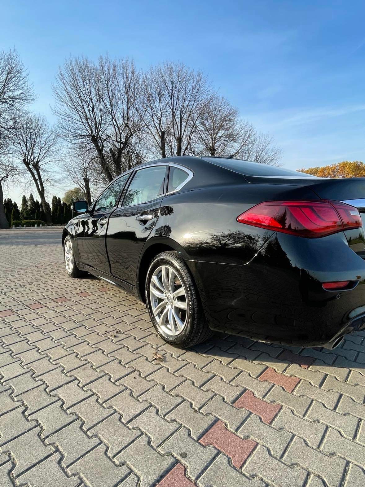 Błyszczący, czarny samochód sedan po detailingu, widoczny z tyłu, zaparkowany na kostce brukowej w słoneczny dzień.