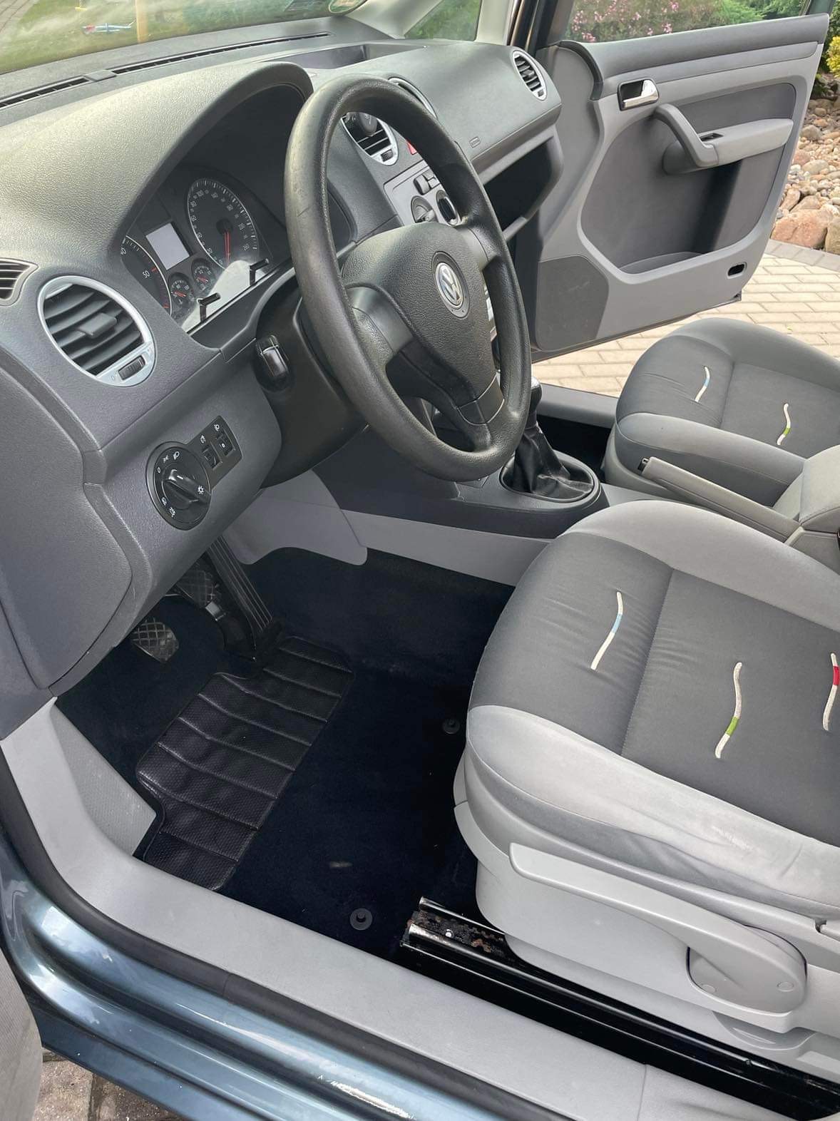 Wnętrze samochodu z czarnymi dywanikami i szaro-czarną tapicerką foteli z dekoracyjnymi przeszyciami w kształcie łuków.