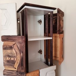 Pawel Manka - Nietypowa szafka wisząca z otwartymi drzwiczkami, wykonana z różnych rodzajów drewna, z widocznymi zawiasami i półkami wewnątrz.
