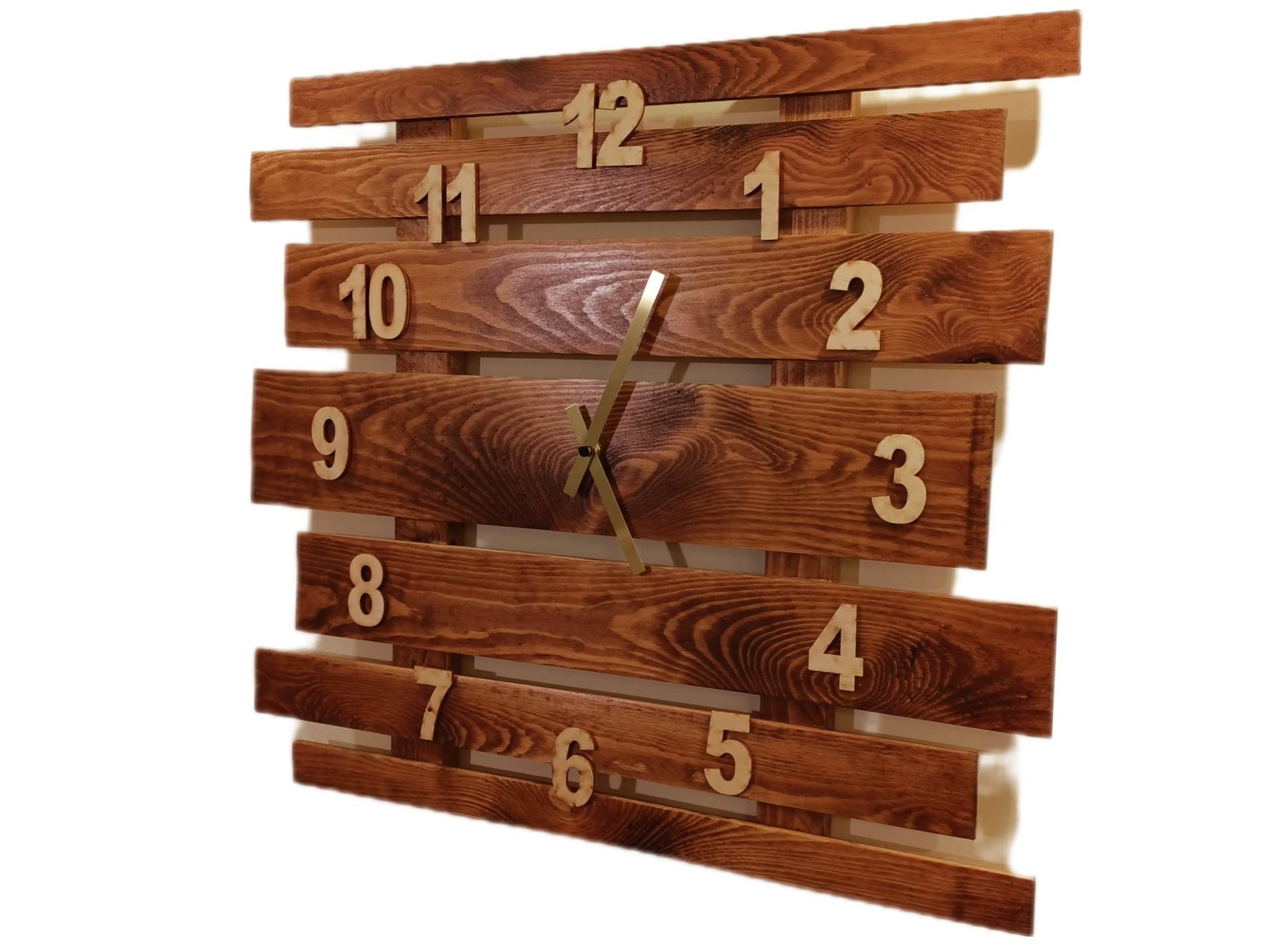 Drewniany zegar ścienny wykonany z poziomych desek w ciepłym odcieniu brązu, z wyciętymi cyframi i złotymi wskazówkami.