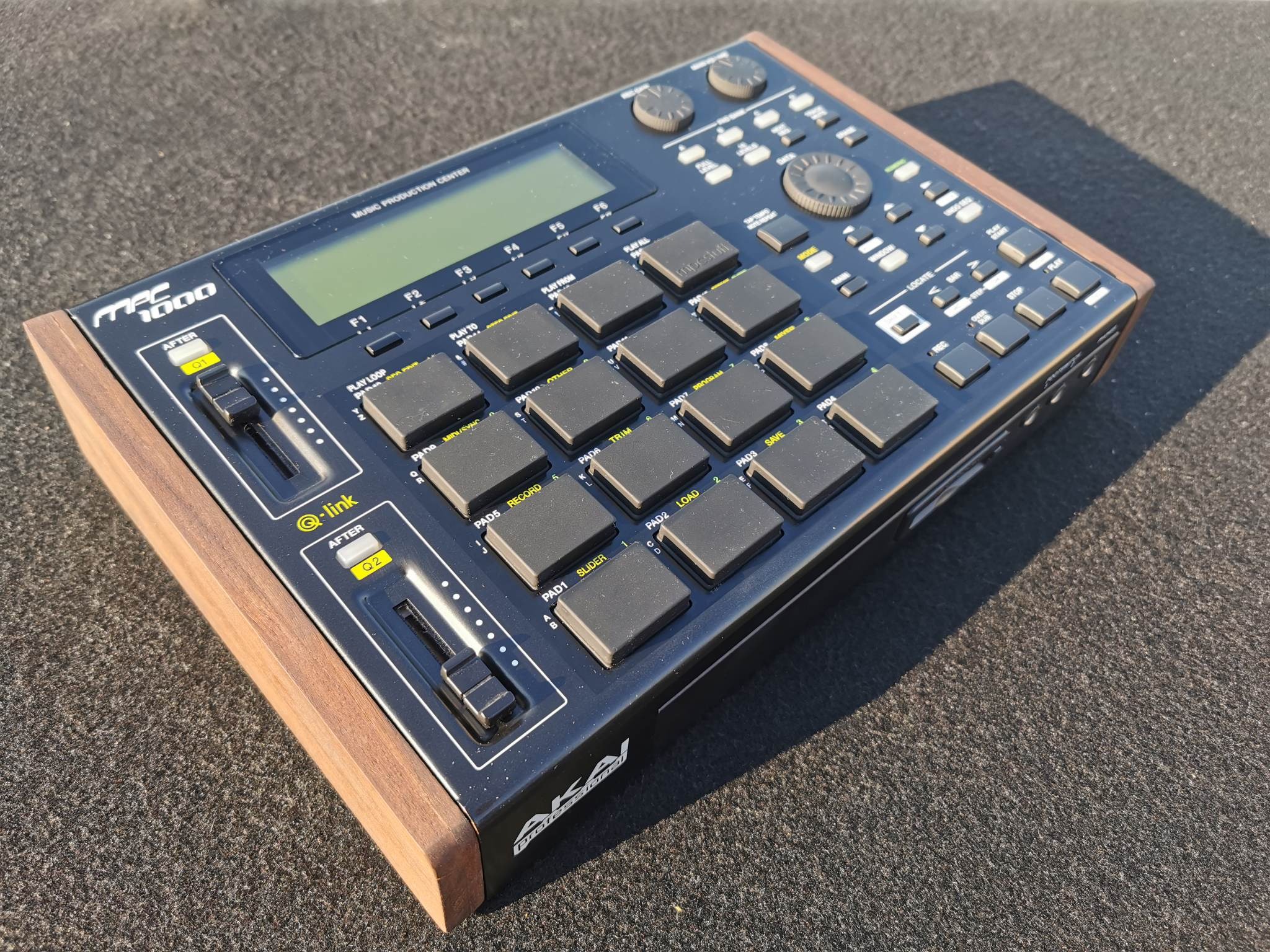 Akai MPC1000 Music Production Center z drewnianymi bokami, leżący na szarej powierzchni, widok z góry.