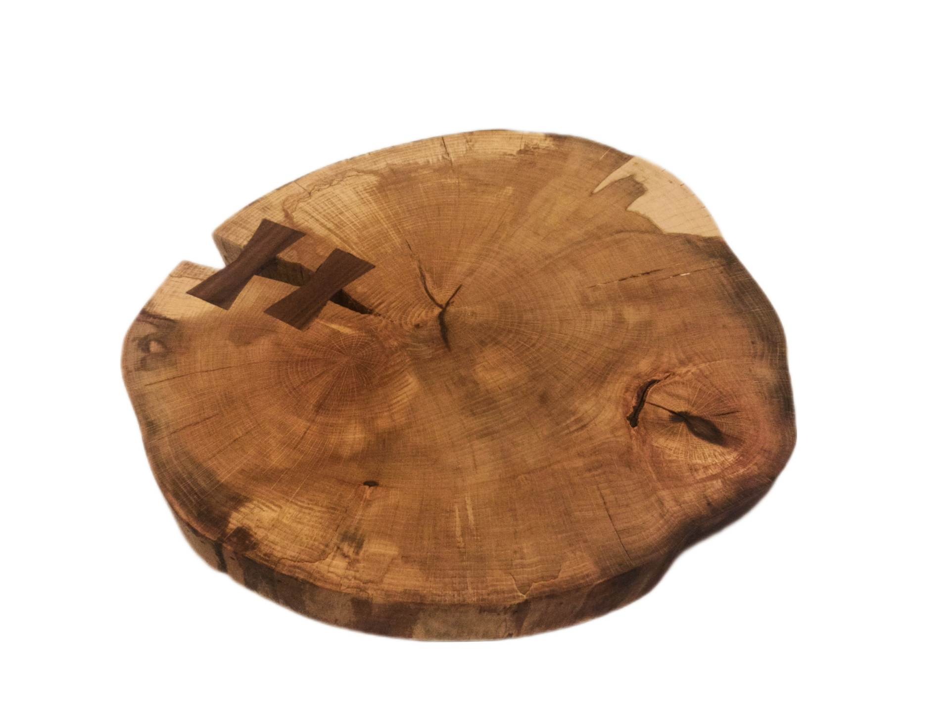 Przekrój pnia drzewa z widocznymi słojami i wstawkami w kształcie litery H z ciemniejszego drewna, tworzącymi dekoracyjny element wzmacniający.