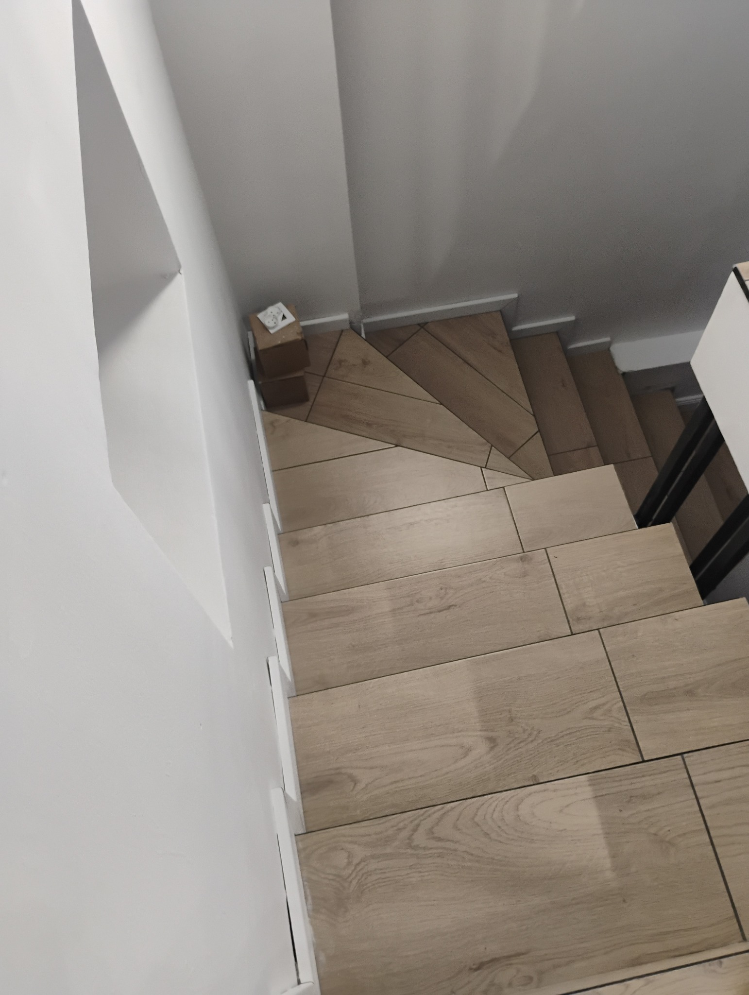 Wykończone schody wyłożone płytkami imitującymi drewno, widok z góry, z małym kartonem na górnym stopniu.