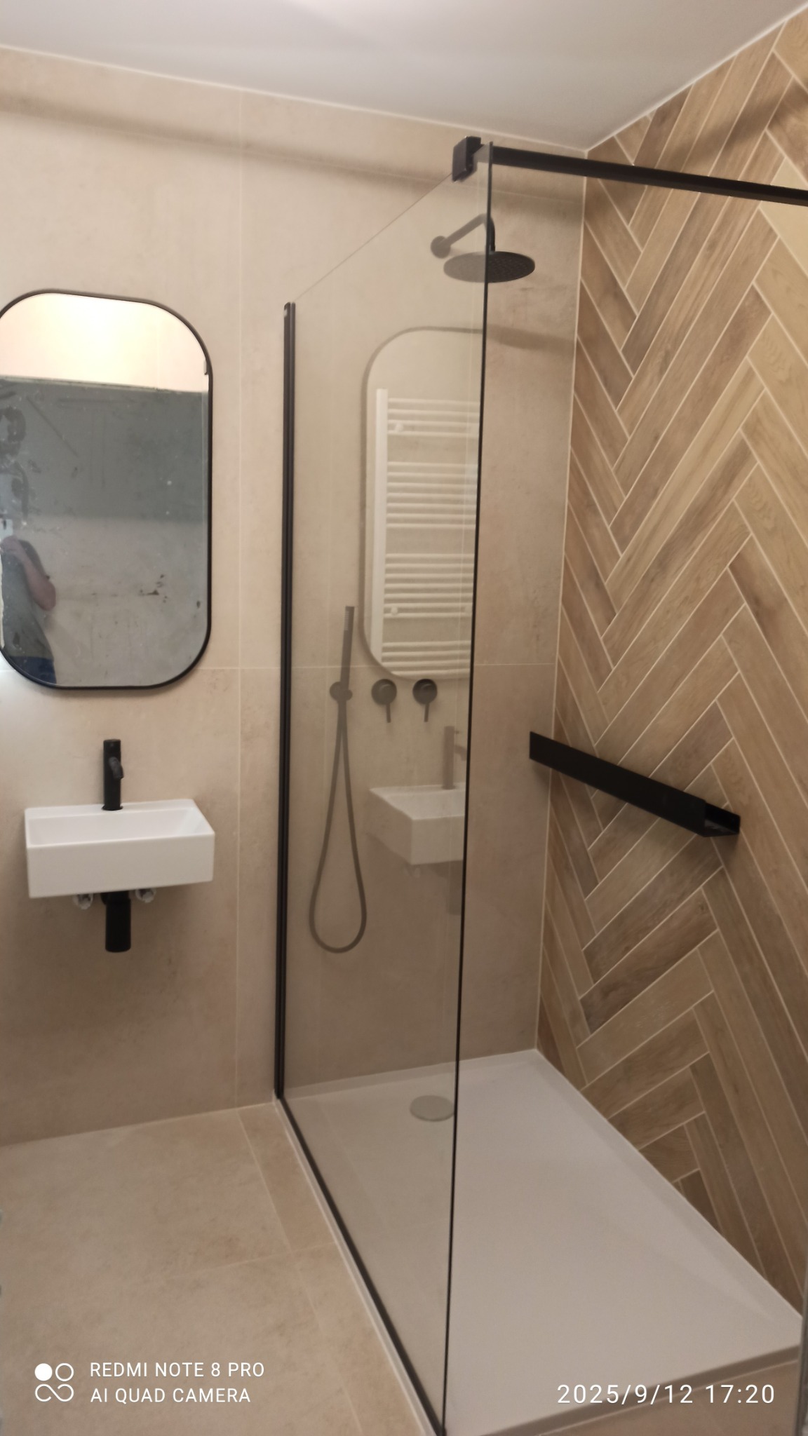 Nowoczesna łazienka z kabiną prysznicową typu walk-in, umywalką nablatową i lustrem w czarnej ramie. Ściana wykończona płytkami imitującymi drewno ułożonymi w jodełkę.