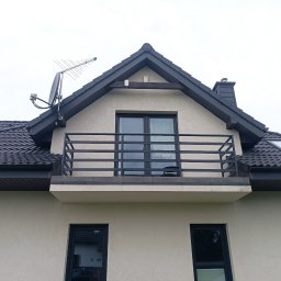 Balustrady, konstrukcje Bydgoszcz i okolice WBO Bartosz Winowiecki - Dom z balkonem zabezpieczonym metalową, czarną balustradą. Na dachu widoczna antena satelitarna i komin. Okna i dach w ciemnej tonacji, elewacja jasna.