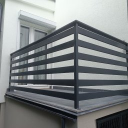 Balustrady, konstrukcje Bydgoszcz i okolice WBO Bartosz Winowiecki - Nowoczesna, szara balustrada balkonowa z poziomych profili, zamontowana na płytkach. Widok z dołu, fragment elewacji budynku z oknem i roletą.