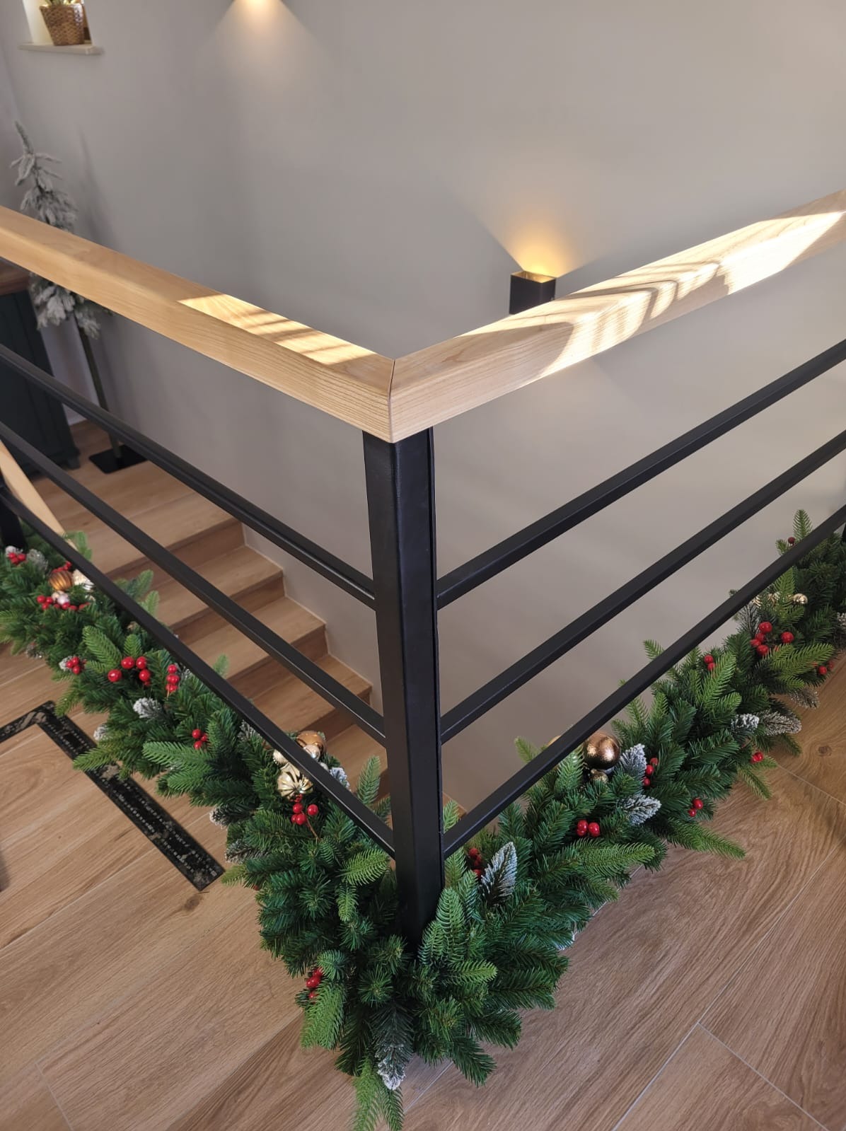 Wewnętrzne schody z metalową balustradą i drewnianym pochwytem, udekorowane świąteczną girlandą z czerwonymi jagodami i złotymi bombkami, widok z góry.
