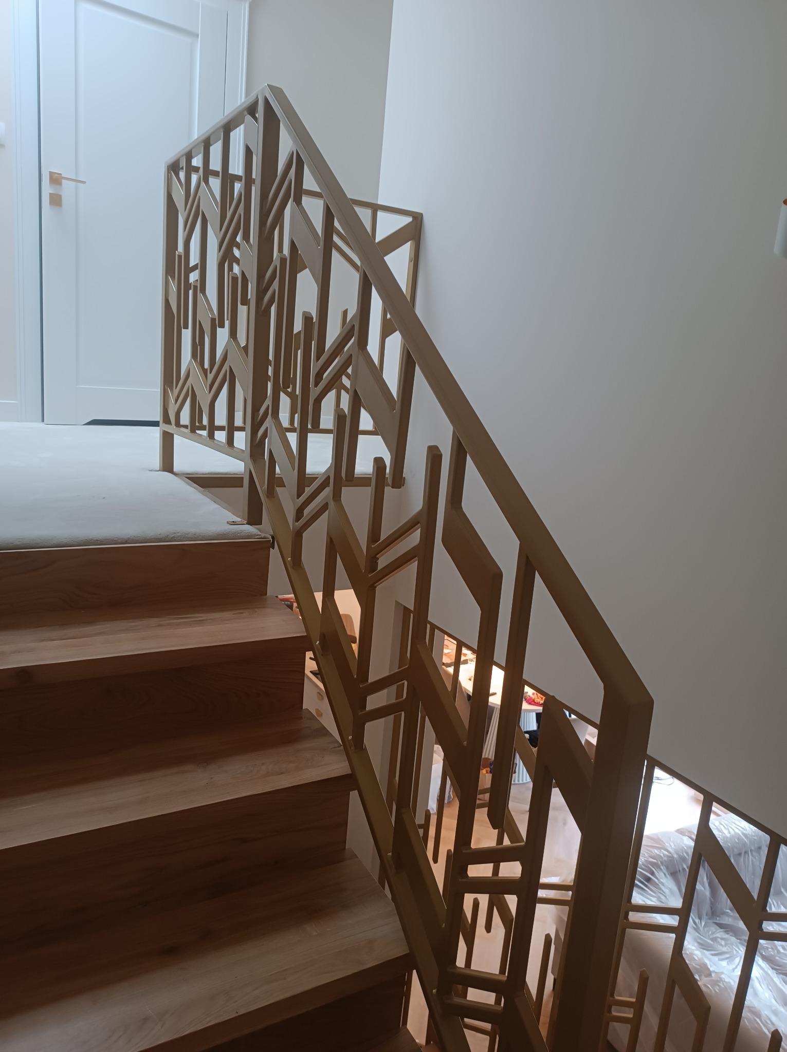 Drewniane schody z ażurową balustradą o geometrycznym wzorze. Widok z góry na stopnie, białe drzwi w tle. Nowoczesny design.