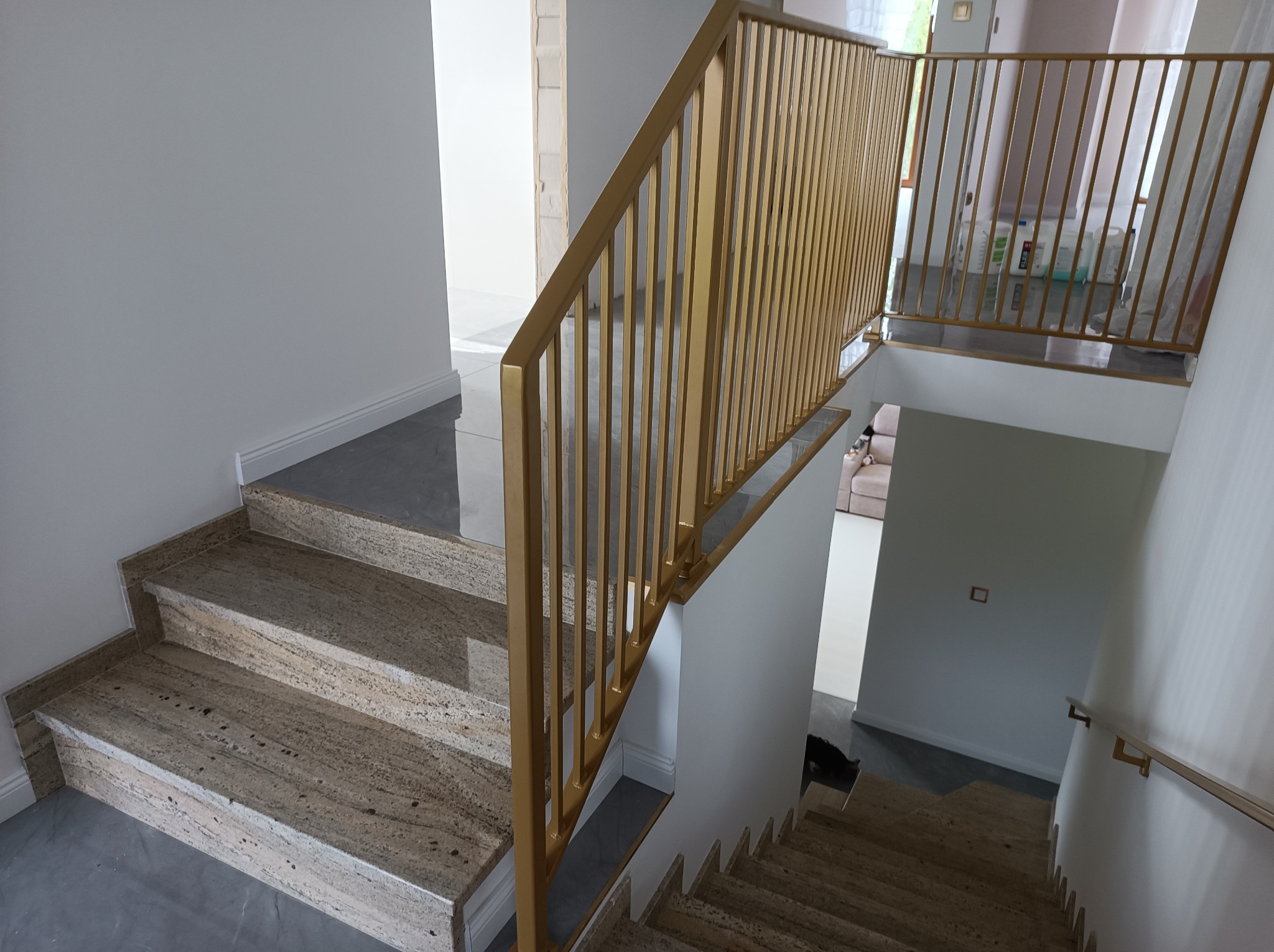 Schody z kamiennymi stopniami i złotą balustradą, widok z góry. Nowoczesny design, jasne wnętrze. Częściowe ujęcie schodów.