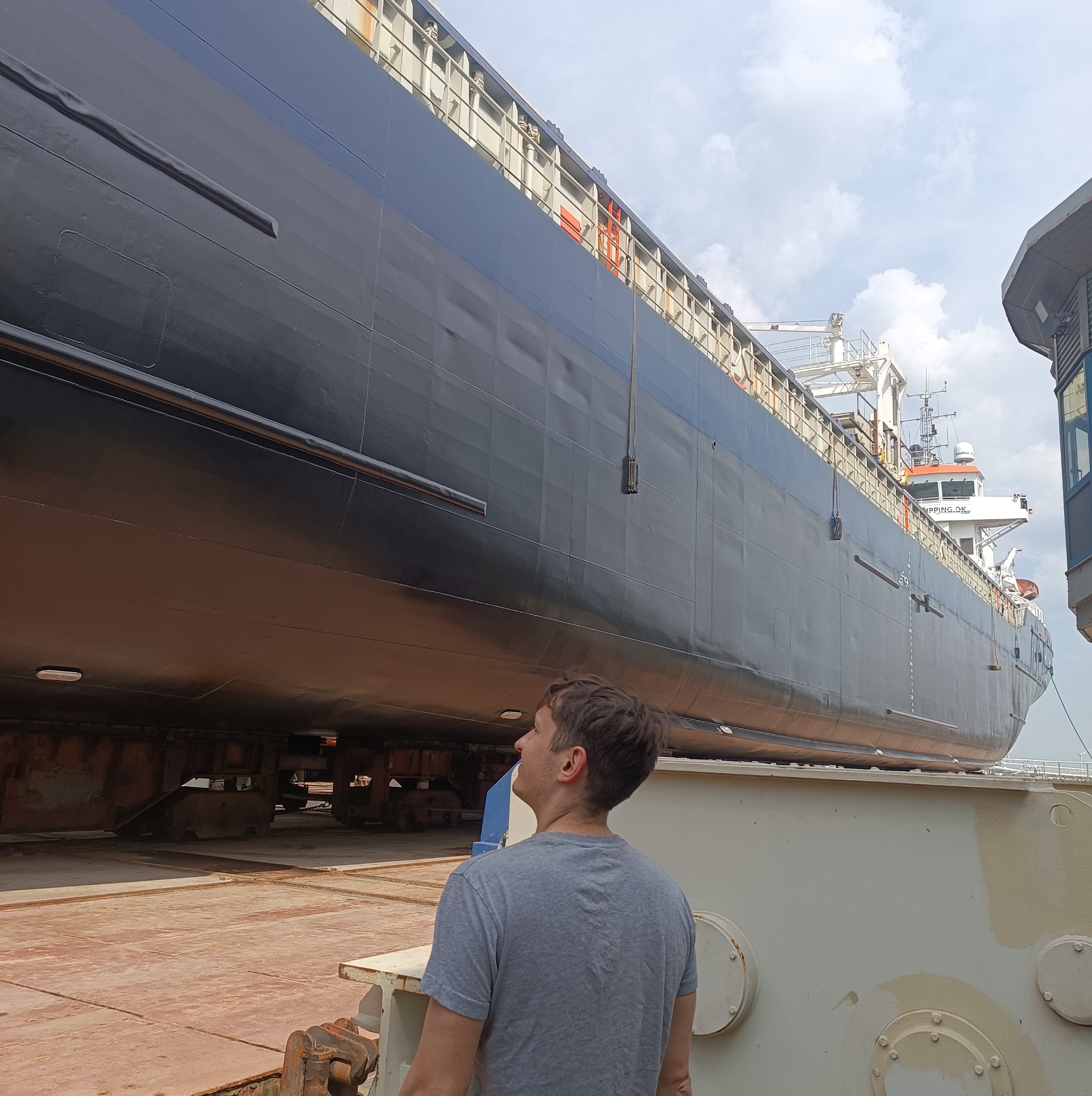 Mężczyzna spogląda na kadłub statku na doku, widoczne detale konstrukcyjne i elementy wyposażenia. Ślusarstwo okrętowe.