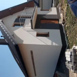 Nowo wykończona elewacja domu jednorodzinnego z balkonem, widoczne fragmenty kostki brukowej przygotowanej do ułożenia.