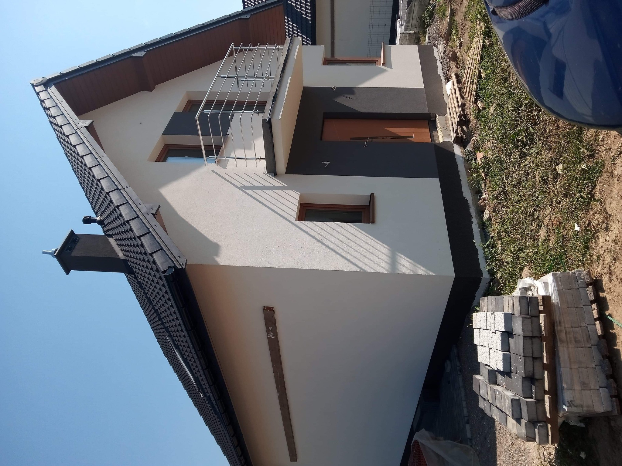 Nowo wykończona elewacja domu jednorodzinnego z balkonem, widoczne fragmenty kostki brukowej przygotowanej do ułożenia.