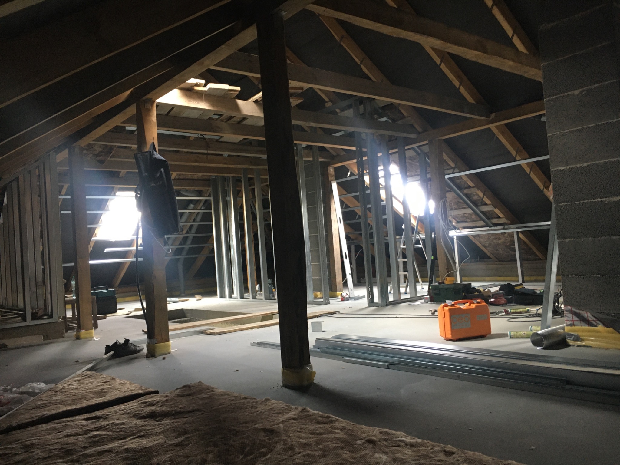 Poddasze w trakcie ocieplania, widoczne krokwie, wełna mineralna, profile metalowe, narzędzia i skrzynka narzędziowa.