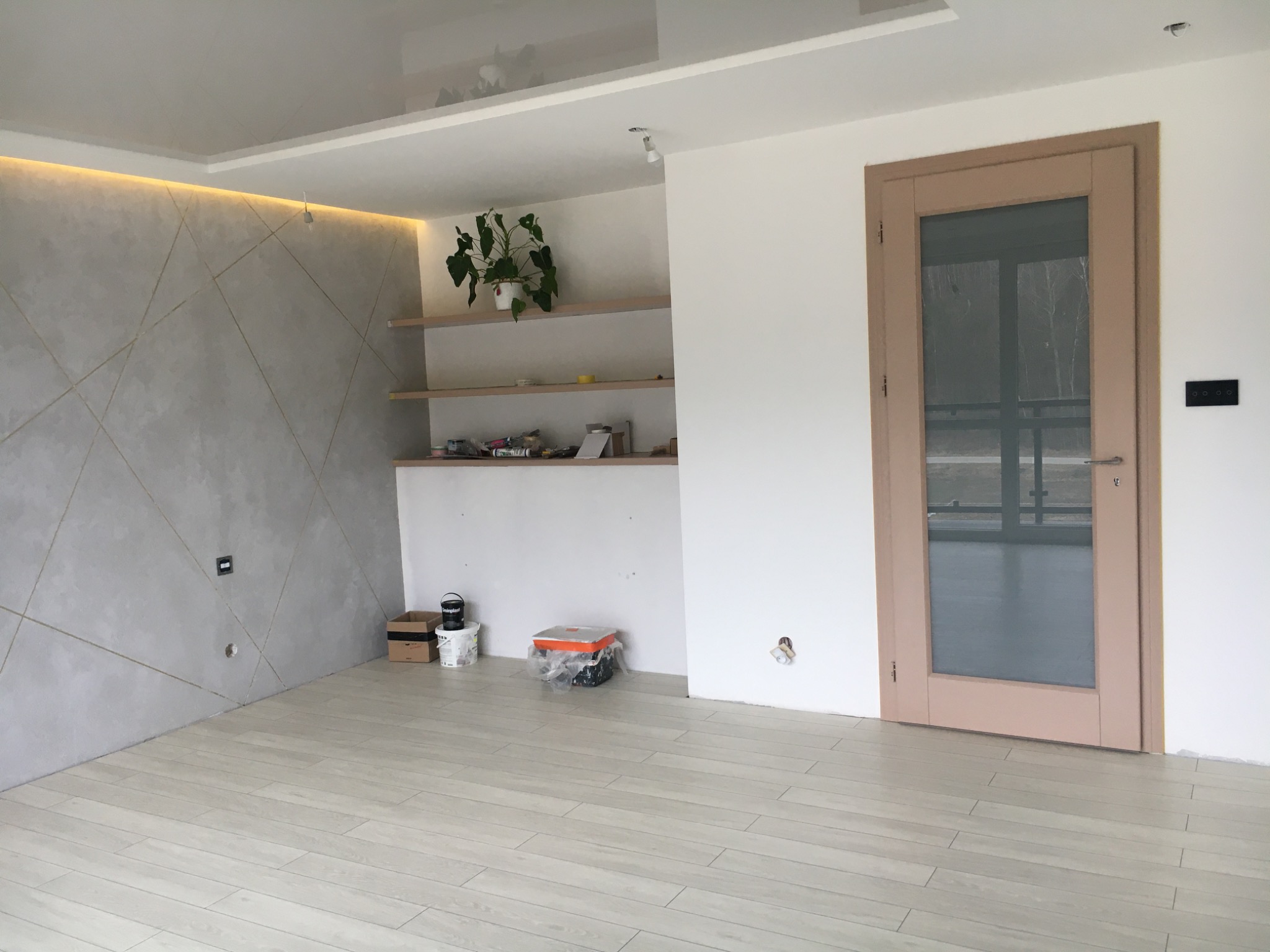 Wnętrze po remoncie w Zamościu: Ściana z dekoracyjną gładzią w geometryczne wzory, drewnopodobna podłoga, drzwi wewnętrzne z przeszkleniem oraz półki z rośliną doniczkową.