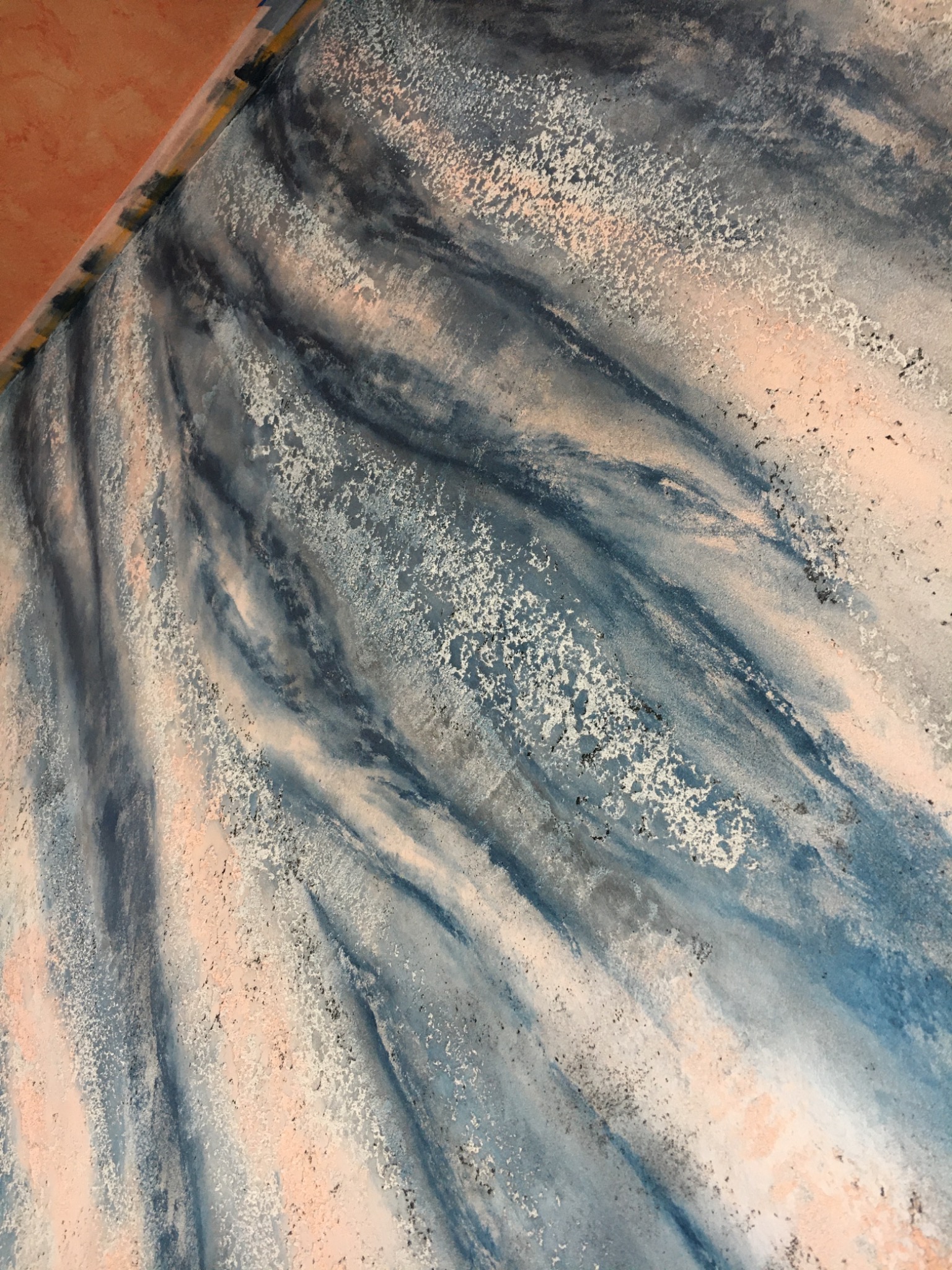 Dekoracyjna ściana z efektem malarskim w odcieniach błękitu, szarości i subtelnej brzoskwini, z wyraźną fakturą i miejscowymi spękaniami.