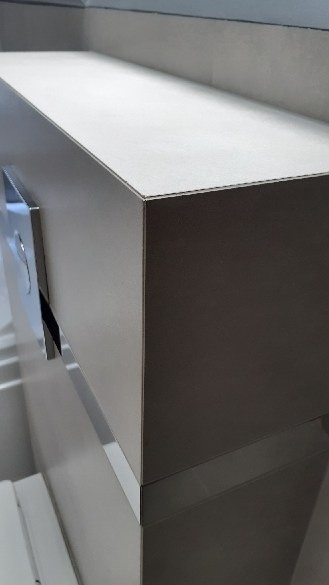 Nowoczesna, minimalistyczna umywalka z blatem w odcieniach szarości i chromowanym dozownikiem mydła, zamontowana w łazience z szarymi płytkami.