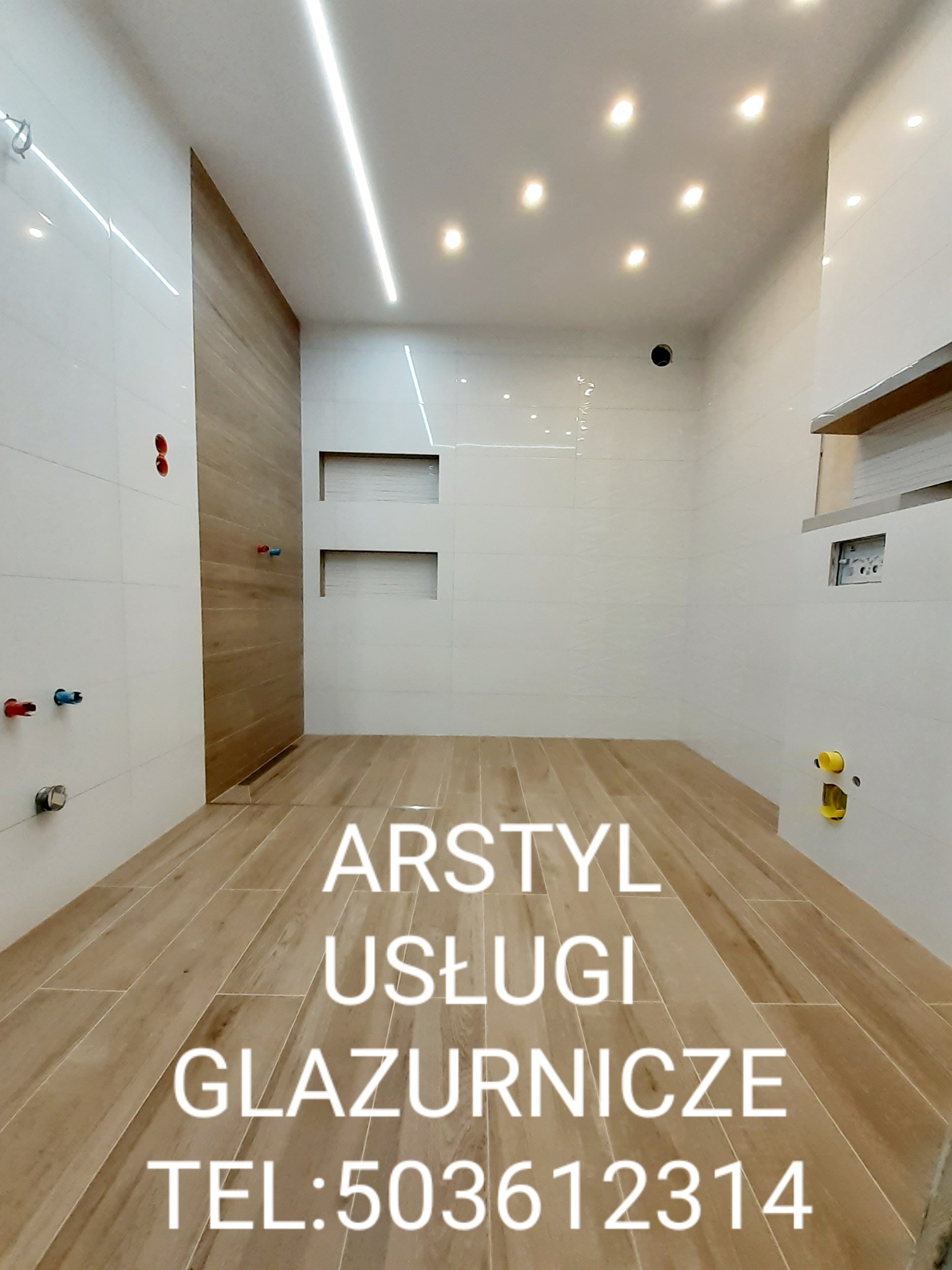 Wnętrze łazienki po remoncie z jasnymi płytkami na ścianach i podłodze imitującymi drewno, z widocznymi instalacjami wodnymi i oświetleniem sufitowym.