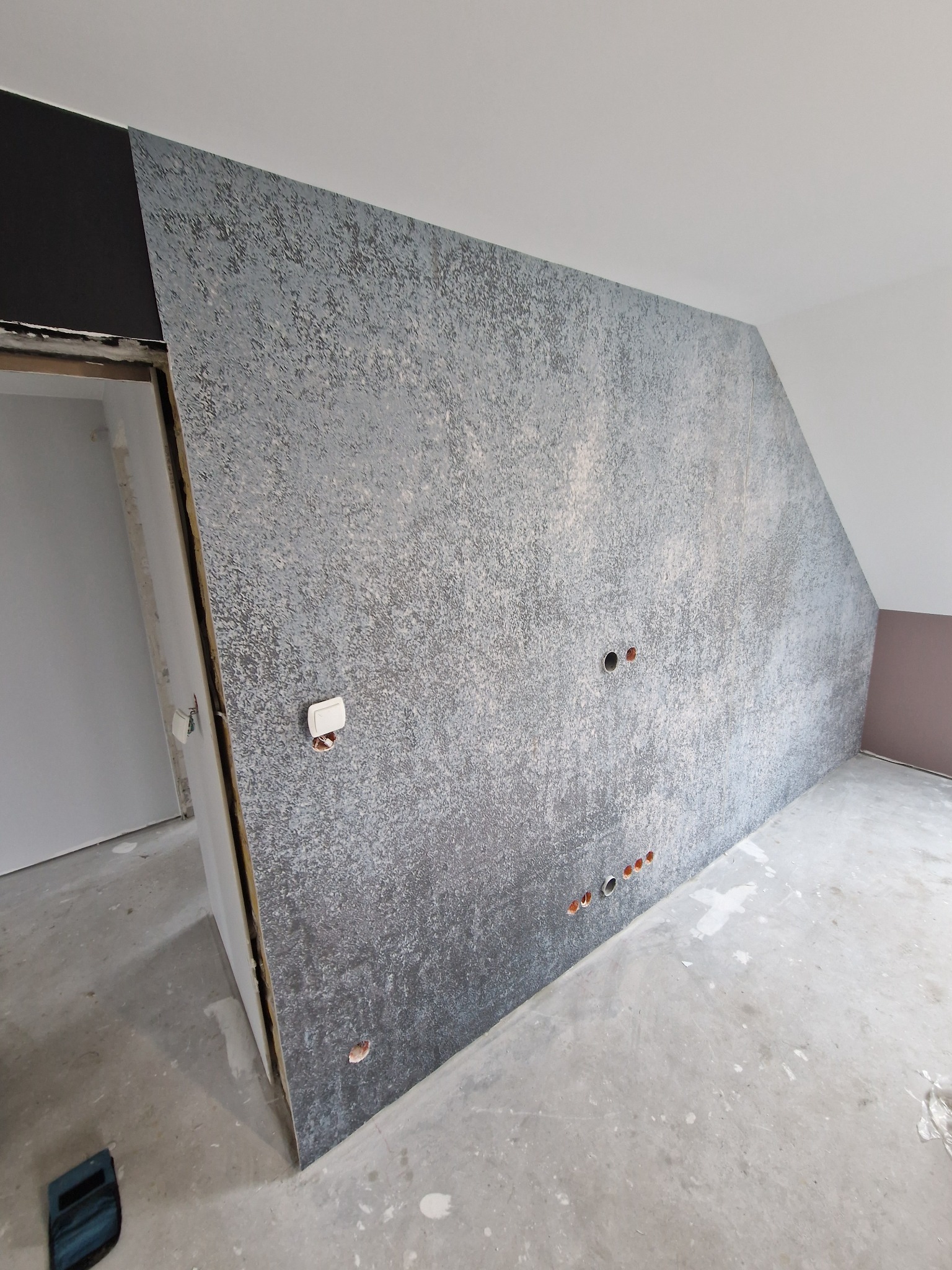 Montaż panelu ściennego imitującego beton, z widocznymi otworami na gniazdka elektryczne, w surowym wnętrzu z widocznym betonowym podłożem.