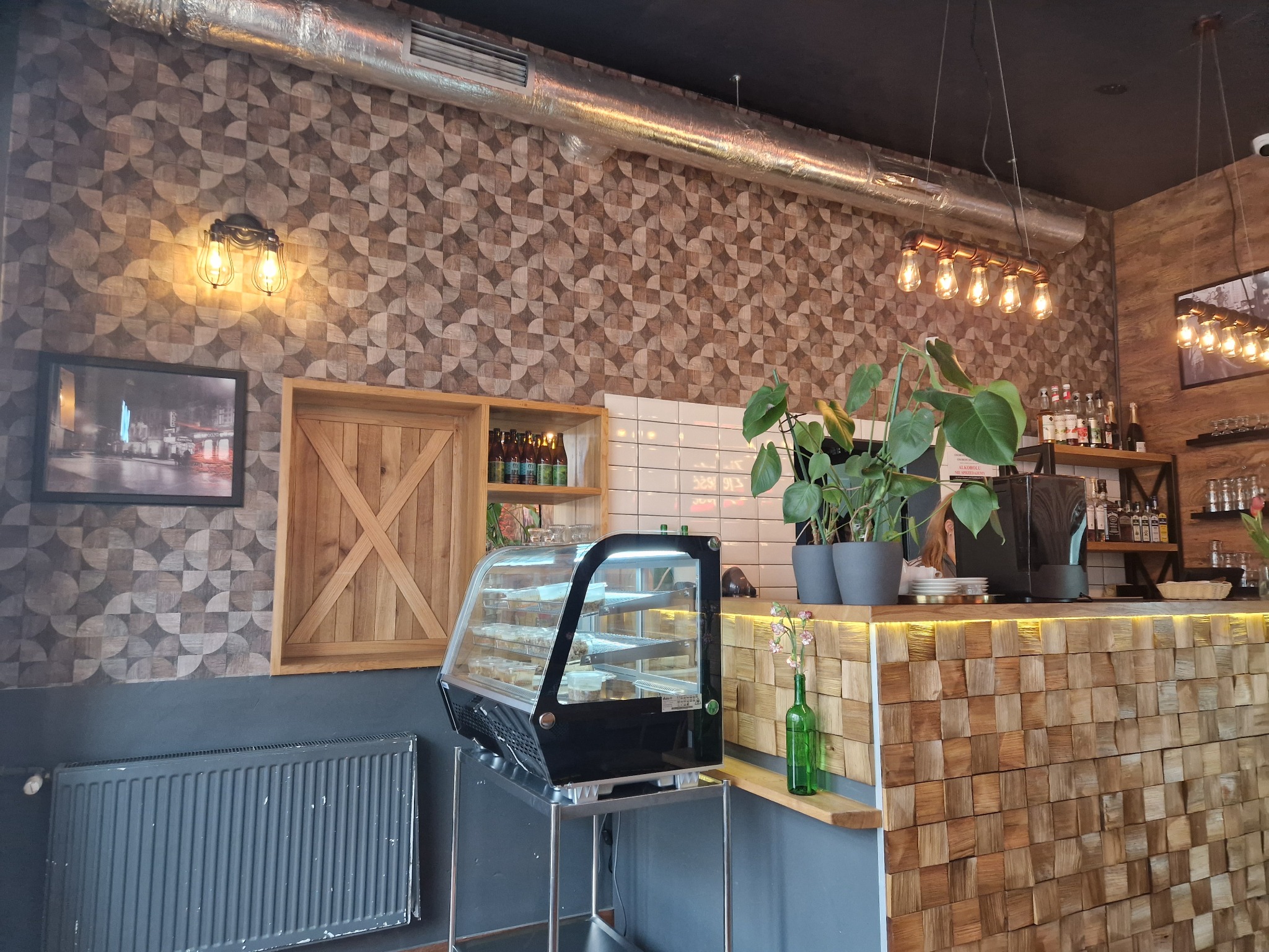 Wnętrze kawiarni z tapetą w geometryczne wzory, drewnianą ladą i dekoracyjnymi lampami