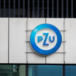 Logo PZU na fasadzie budynku z metalowymi elementami, widoczne odbicie budynku w dolnych oknach.