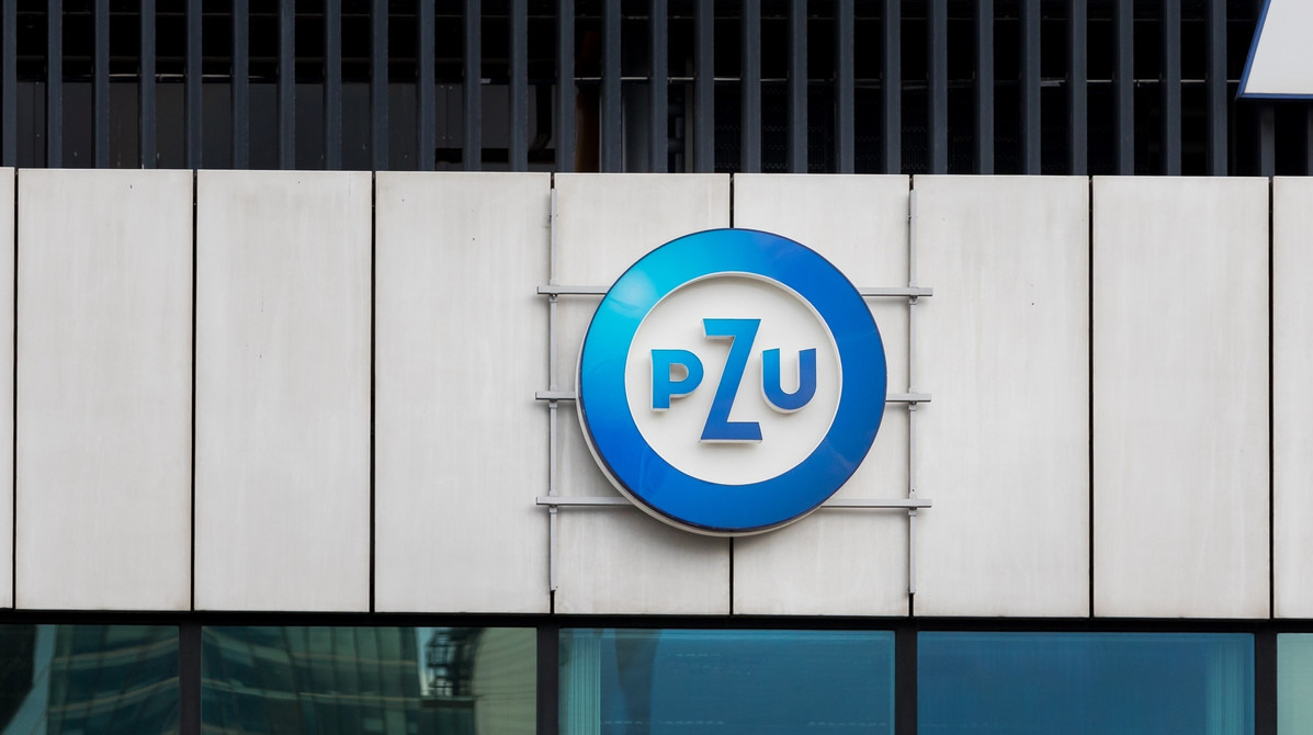Logo PZU na fasadzie budynku z metalowymi elementami, widoczne odbicie budynku w dolnych oknach.