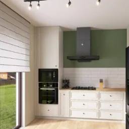 Wnętrze kuchni z białymi szafkami, drewnianym blatem, czarnym sprzętem AGD i zieloną ścianą, oświetlone punktowymi lampami sufitowymi i światłem dziennym przez okno z roletą rzymską.