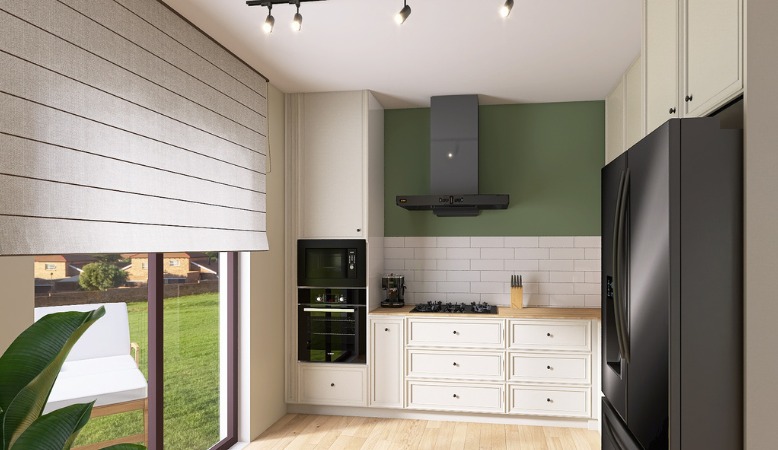 Wnętrze kuchni z białymi szafkami, drewnianym blatem, czarnym sprzętem AGD i zieloną ścianą, oświetlone punktowymi lampami sufitowymi i światłem dziennym przez okno z roletą rzymską.